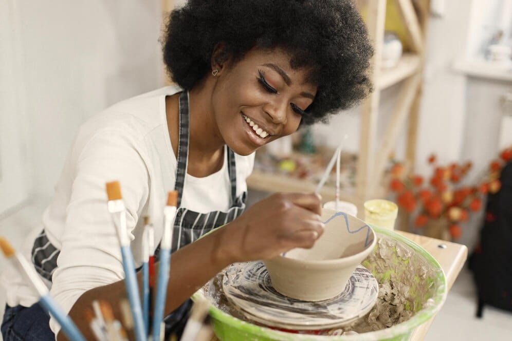 young black woman painting clay pot art studio craftswoman painting ceramic bowl workbench girl wearing blue apron 1157 51482